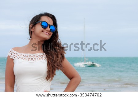 Young woman posing on the beach with boat in the sea in the background.