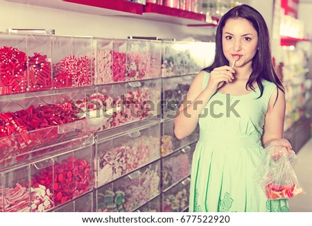 Young woman posing to photographer picking different candies with  scoop in  cellophane bag
