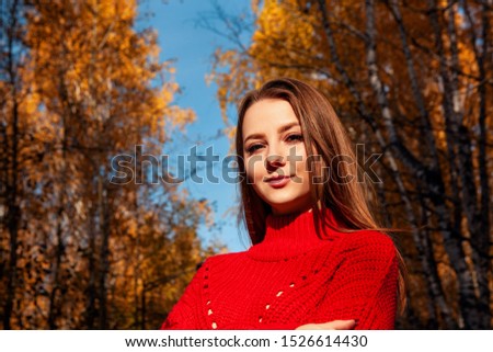 Young woman posing in red sweater over yellow leaves background in autumn.