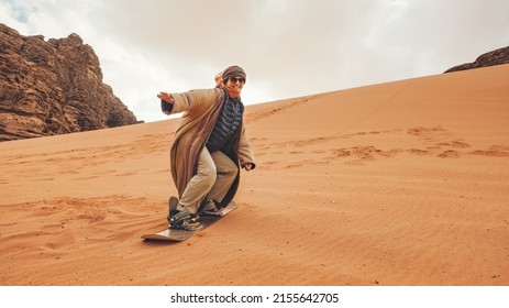 Young Woman Posing As Sand Dune Surfing Wearing Bisht - Traditional Bedouin Coat. Sandsurfing Is One Of The Attractions In Wadi Rum Desert