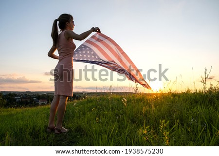Young woman posing with USA national flag outdoors at sunset. Positive female celebrating United States independence day.