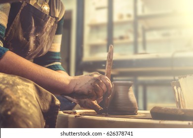 Young woman potter in apron at work. Craftsman artist shapes the jug with his hands and a special tool on pottery wheel. Copy space, toned - Powered by Shutterstock