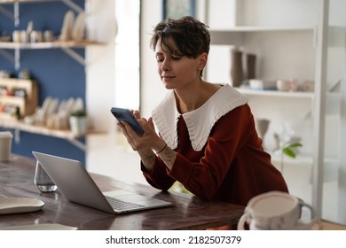 Young woman pottery store manager using mobile phone at workplace, female ceramics artist connecting with customer through social media, craftswoman with smartphone promoting craft business online - Powered by Shutterstock