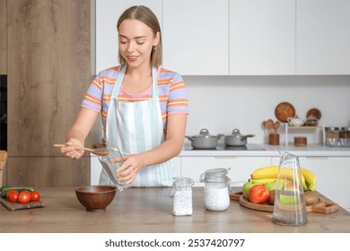 Young woman pouring chia seeds into glass in kitchen - Powered by Shutterstock