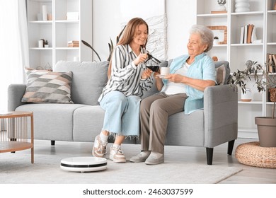 Young woman pouring coffee for her grandmother with robot vacuum cleaner at home - Powered by Shutterstock