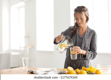 Young woman pouring fresh lemonade from jug into glass at home - Powered by Shutterstock