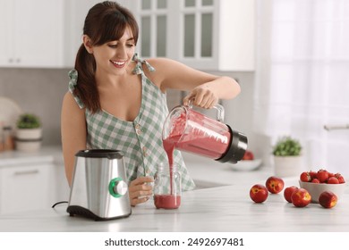 Young woman pouring fresh smoothie from blender cup into glass at white marble table in kitchen - Powered by Shutterstock