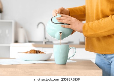 Young woman pouring hot tea into cup in kitchen, closeup - Powered by Shutterstock