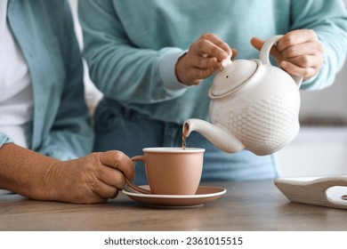 Young woman pouring hot tea for her mother in kitchen, closeup