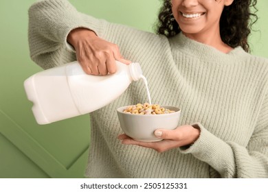 Young woman pouring milk into bowl of cereal rings against color wall, closeup - Powered by Shutterstock