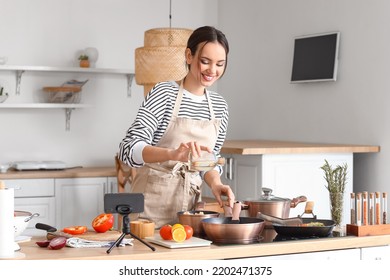 Young woman pouring oil onto frying pan while following cooking video tutorial in kitchen - Powered by Shutterstock