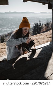 A Young Woman Pouring Out Coffee From A Moka Pot Into A Cup In Outdoors House In Front Of A Mountains Landscape