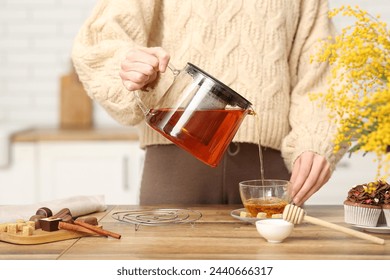 Young woman pouring tea with honey from teapot into cup in kitchen - Powered by Shutterstock