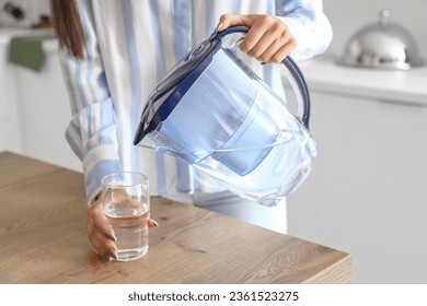 Young woman pouring water from filter jug into glass in kitchen, closeup