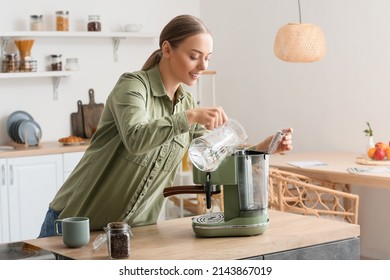 Young Woman Pouring Water Into Coffee Machine In Kitchen