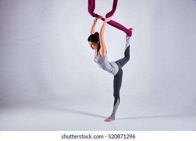 Young woman practices aerial different inversion anti-gravity yoga with a hammock in a white studio. Concept of a mental and physical health an harmony living - Powered by Shutterstock