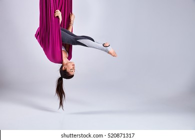 Young woman practices aerial different inversion anti-gravity yoga with a hammock in a white studio. Concept of a mental and physical health an harmony living