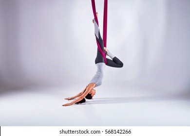 Young woman practices aerial different inversion anti-gravity yoga with a hammock in a white studio. Concept of a mental and physical health and harmony living