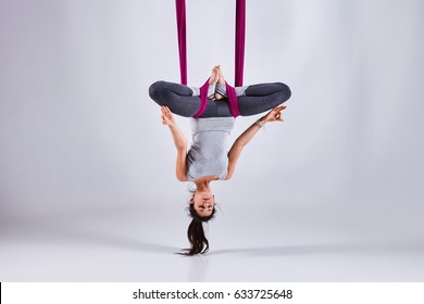 Young woman practices aerial different inversion anti-gravity yoga with a hammock in a white studio. Concept of a mental and physical health and harmony living