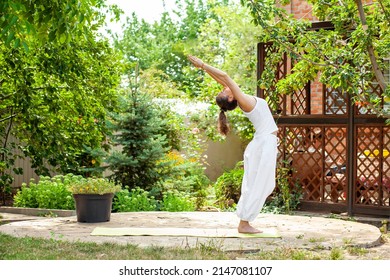 Young woman practices yoga in the garden. Deflection in the practice of surya namaskar. Tadasana - Mountain pose with stretched hands