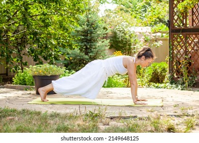 Young woman practices yoga in the garden. Surya namaskar, Plank exercise. Upper chaturanga dandasana