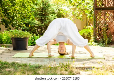 Young Woman Practices Yoga In The Garden. Prasarita Padottanasana Or Wide Stance Forward Bend.