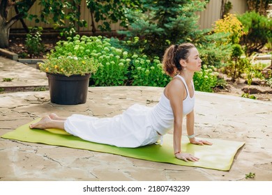 Young woman practices yoga in the garden. Surya namaskar, Bhujangasana Cobra Pose.