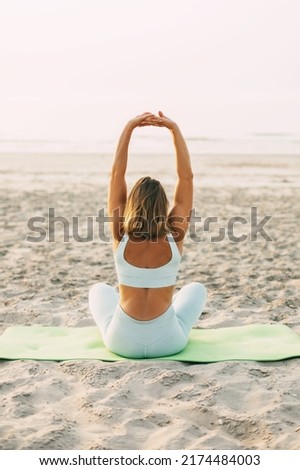 A young woman practices yoga in the lotus position on the shore of the poria, rear view