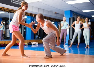 Young woman practicing basic self-defense techniques while training in gym with male partner, performing supinating wristlock