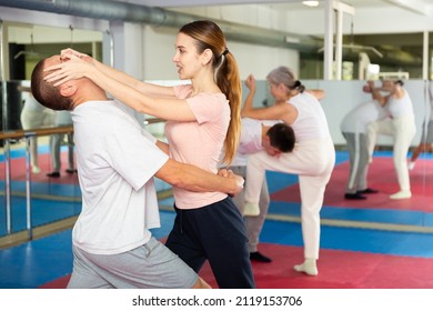 Young woman practicing basic self-defense moves during training at gym with male partner, using painful technique for eyes to opponent