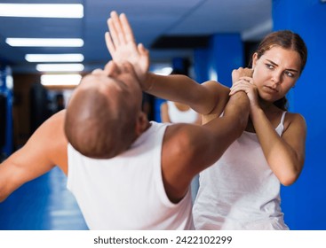 Young woman practicing basic self-defense techniques while training in gym with male partner, performing palm heel strike in chin - Powered by Shutterstock