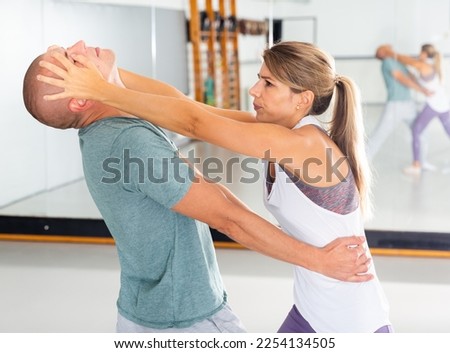 Young woman practicing basic self-defense moves during training at gym with male partner, using painful technique for eyes of opponent..