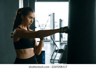 Young woman practicing boxing at the gym, she wears boxing gloves and hits a punching bag. - Powered by Shutterstock