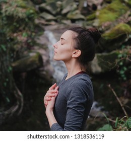 Young woman practicing breathing yoga pranayama outdoors in moss forest on background of waterfall. Unity with nature concept