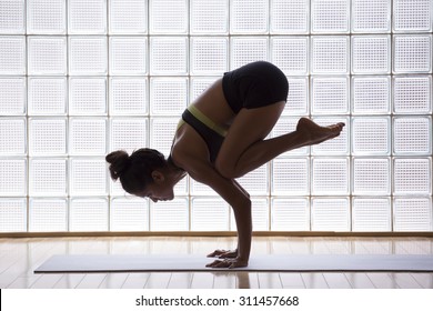 Young woman practicing crow pose in a yoga studio indoors - Powered by Shutterstock