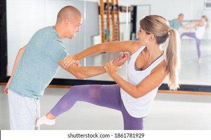 Young Woman Practicing Effective Self-defense Techniques While Training In Gym With Male Partner, Performing Groin Kick