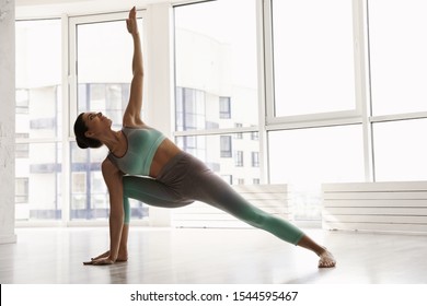 Young woman practicing extended side angle asana in yoga studio. Utthita Parsvakonasana pose - Shutterstock ID 1544595467