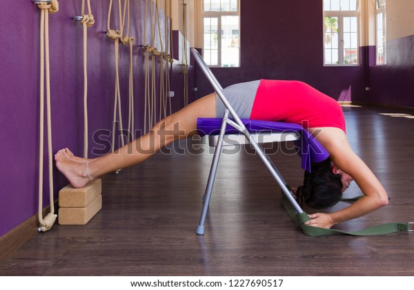 Young woman\
practicing Iyengar yoga using chair and blocks on purple studio.\
Female yogi in urdhva dhanurasana or back bend with props.\
Flexibility, healthy exercise\
concepts