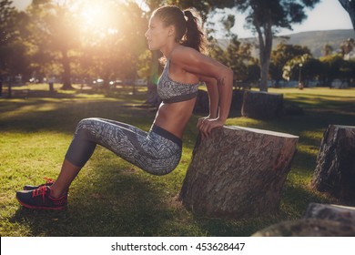 Young woman practicing push ups in a park. Side view shot of muscular female exercising with a log.