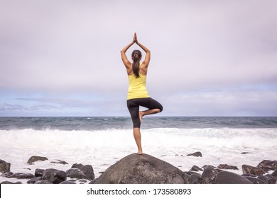 Young woman practicing tree yoga pose near the ocean during sunset