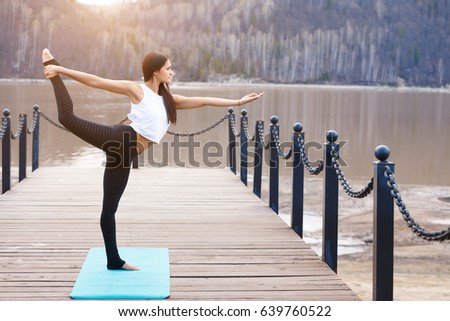 Young woman is practicing yoga at bay nature lake on sunrise