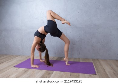 Young woman practicing yoga doing stretching exercises at home during quarantine. Minimalistic empty interior, concrete wall.