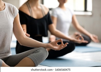 Young woman practicing yoga at group lesson, doing Sukhasana exercise, people sitting in Easy Seat pose, mudra hands close up, stress relief and wellbeing, working out in modern yoga center club