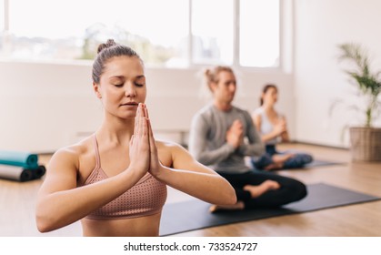 Young woman practicing yoga in gym class in fitness center with people in background. People meditating at health club. - Powered by Shutterstock