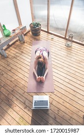 Young woman is practicing yoga at home. She is stretching her back and hamstrings in seated forward fold pose. Girl is following online yoga course. - Shutterstock ID 1720015987