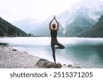 Young woman is practicing yoga at mountain lake. Girl doing yoga on nature. Healthy lifestyles. Concept of vitality, balance, mindfulness, zen energy, calmness, relaxation.