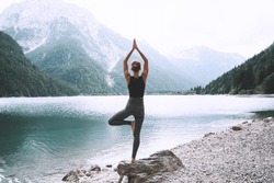 Young Woman Is Practicing Yoga At Mountain Lake. Girl Doing Yoga On Nature. Healthy Lifestyles. Concept Of Vitality, Balance, Mindfulness, Zen Energy, Calmness, Relaxation.
