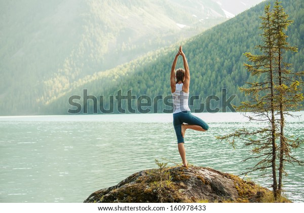 Young woman is\
practicing yoga at mountain\
lake