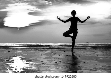 Young Woman Practicing Yoga On The Beach At Sunset (Black And White Photo)