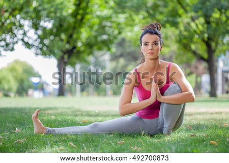 Young woman practicing yoga in the park on the green grass with fallen leaves in autumn with blurred background. Shallow depth of field